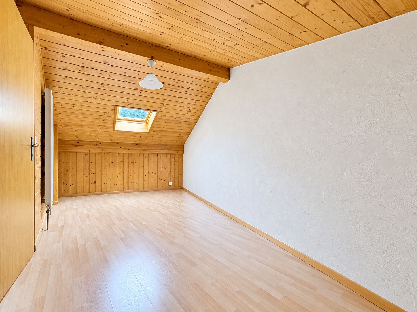 Une chambre mansardée à l'étage, lambris et fenêtre de toit.