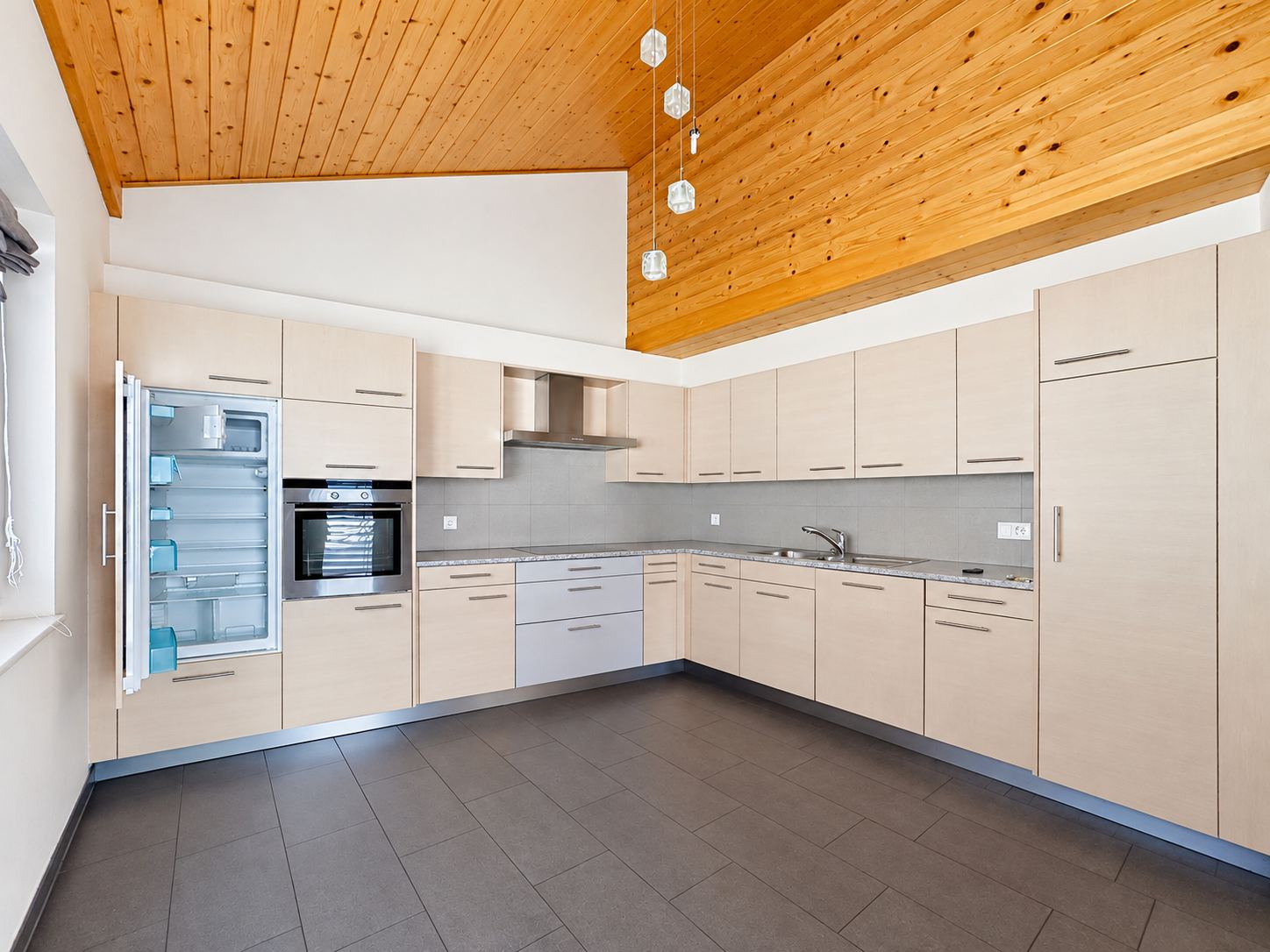 La cuisine équipée en angle : four, réfrigérateur encastré, hotte et nombreux rangements.