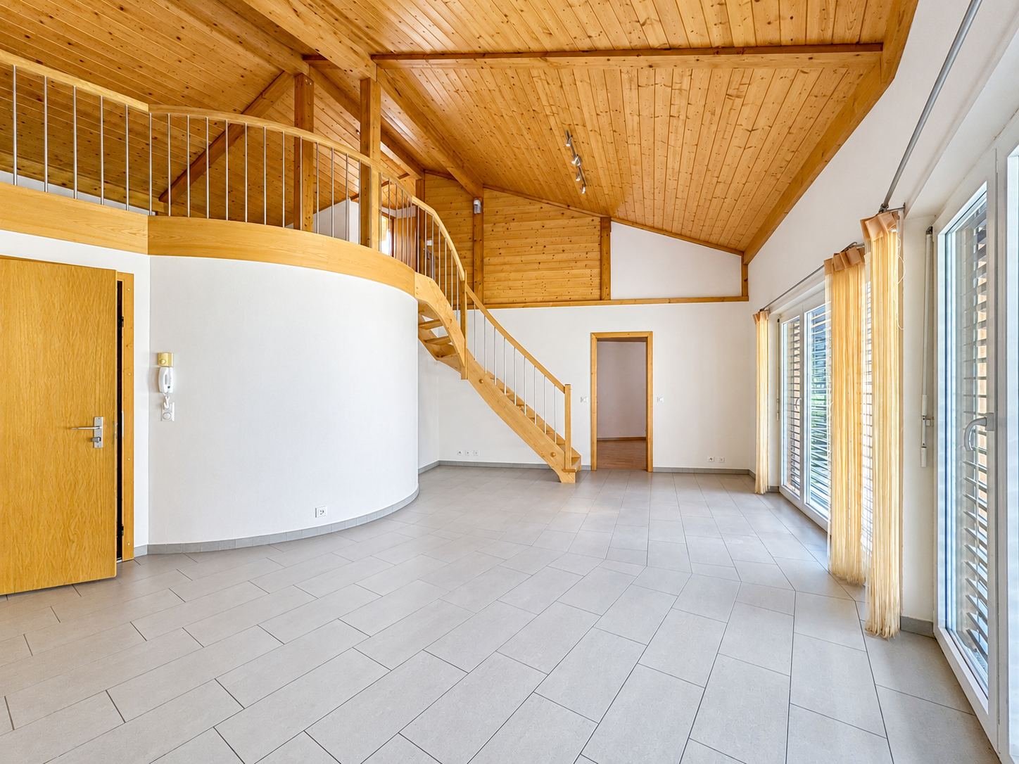 Le séjour en double hauteur, la mezzanine en arrondi et l'escalier en bois.